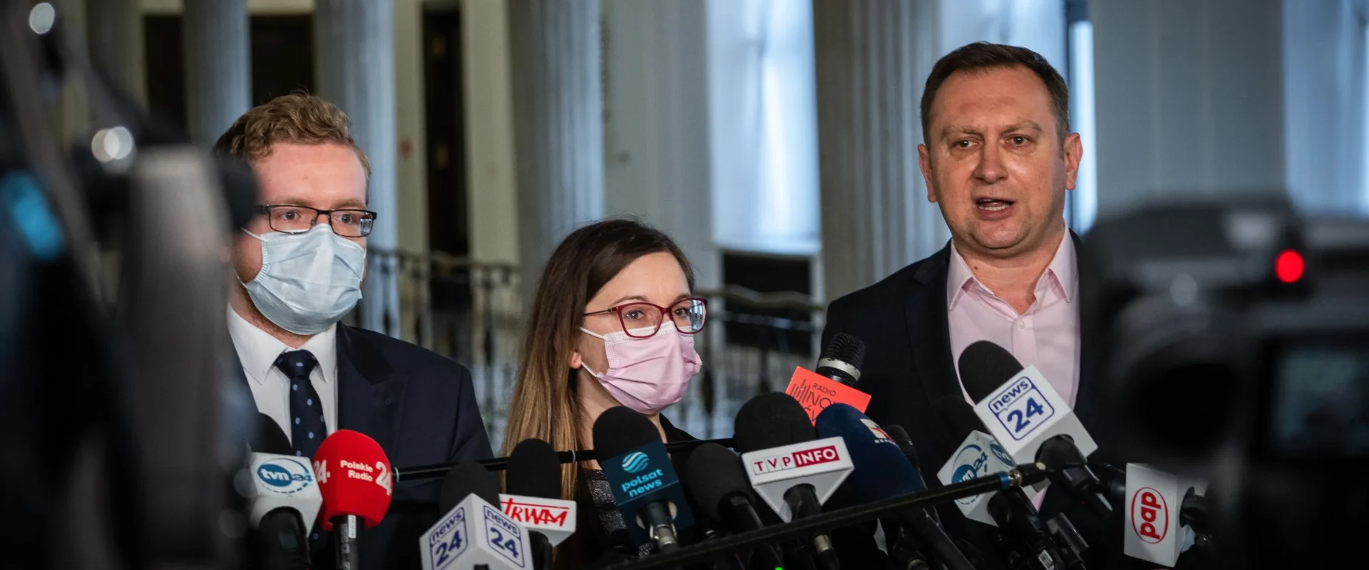 Grupa polityków na konferencji prasowej dotyczącej tarczy antyinflacyjnej, stojąca przed licznymi mikrofonami i kamerami.