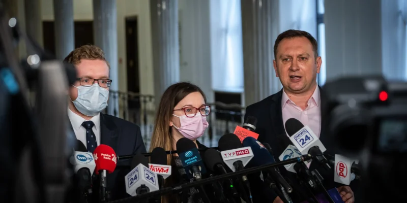 Grupa polityków na konferencji prasowej dotyczącej tarczy antyinflacyjnej, stojąca przed licznymi mikrofonami i kamerami.