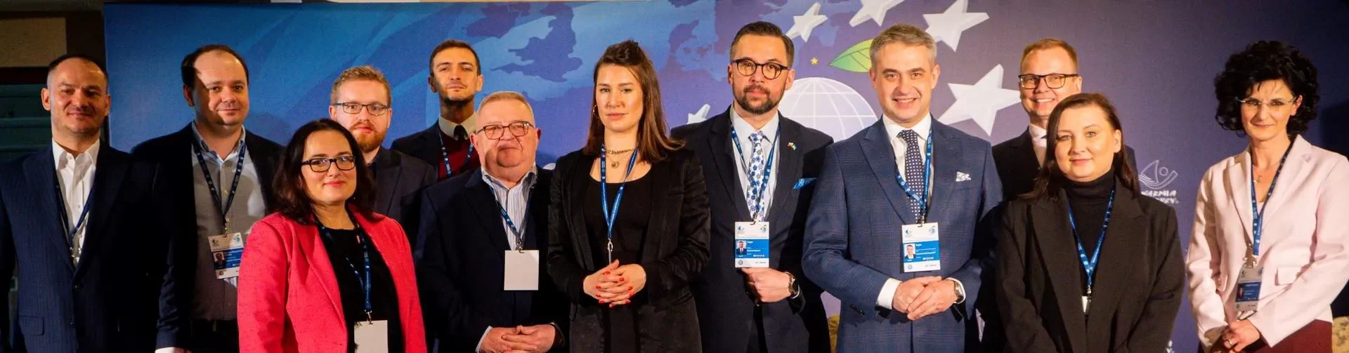 Grupa kilkunastu przedstawicieli samorządów w garniturach i marynarkach stoi razem na tle niebieskiego dekoracyjnego tła podczas Europejskiego Kongresu Samorządów.