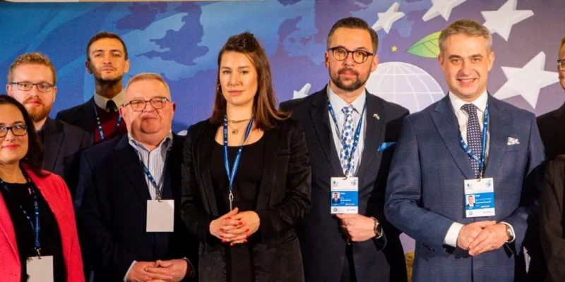 Grupa kilkunastu przedstawicieli samorządów w garniturach i marynarkach stoi razem na tle niebieskiego dekoracyjnego tła podczas Europejskiego Kongresu Samorządów.