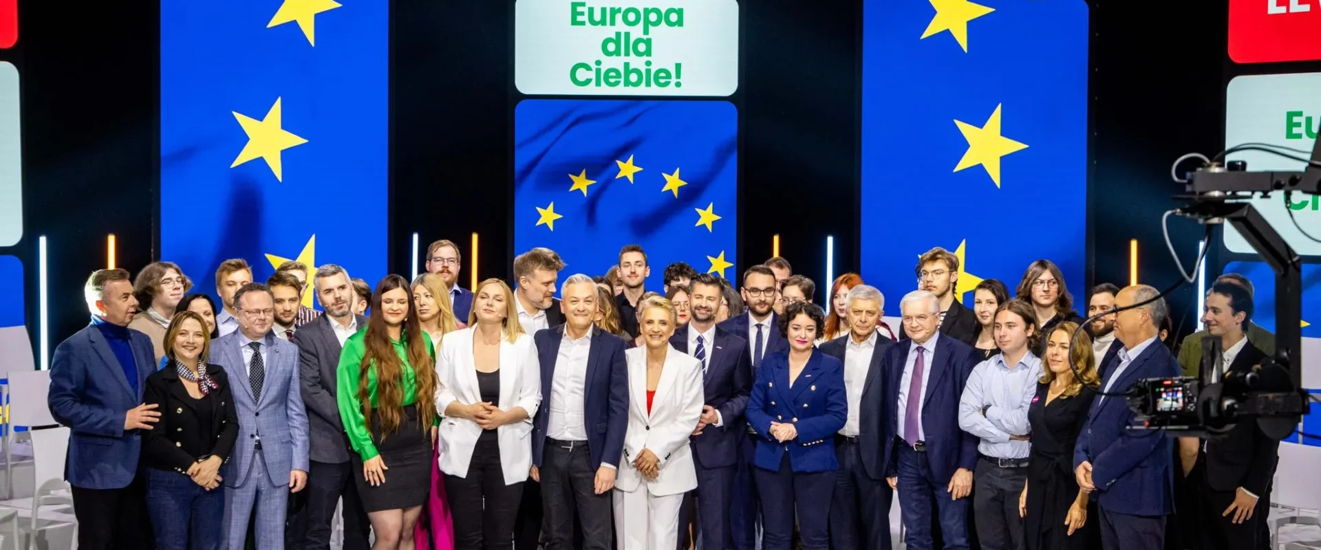 Grupa liderów Lewicy stoi razem na scenie podczas kampanii do Parlamentu Europejskiego, z tyłu kolorowe panele z symbolem Unii Europejskiej i napisem Lewica.