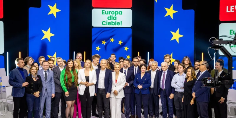 Grupa liderów Lewicy stoi razem na scenie podczas kampanii do Parlamentu Europejskiego, z tyłu kolorowe panele z symbolem Unii Europejskiej i napisem Lewica.