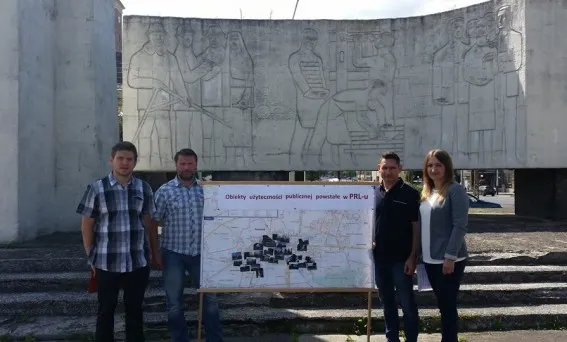 Cztery osoby stoją przed Pomnikiem Bojowników o Wyzwolenie Społeczne i Narodowe, prezentując planszę z mapą obiektów z PRL w ramach protestu przeciw jego wyburzeniu.