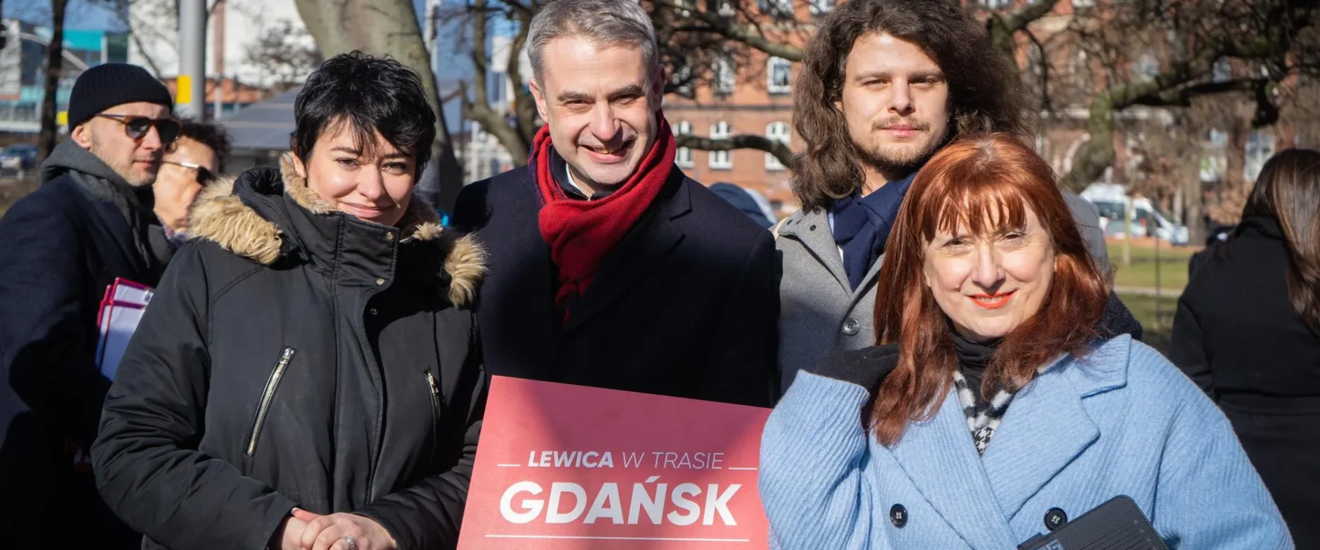 Grupa osób pozująca do zdjęcia na zewnątrz, trzymająca znak z napisem "LEWICA W TRASIE GDAŃSK".
