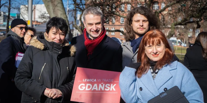 Grupa osób pozująca do zdjęcia na zewnątrz, trzymająca znak z napisem "LEWICA W TRASIE GDAŃSK".