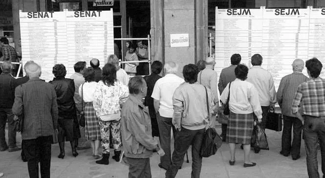 Czarno-białe zdjęcie ludzi stojących przed tablicami z opublikowanymi wynikami wyborów do Senatu i Sejmu, nawiązujące do rocznicy 4 czerwca.