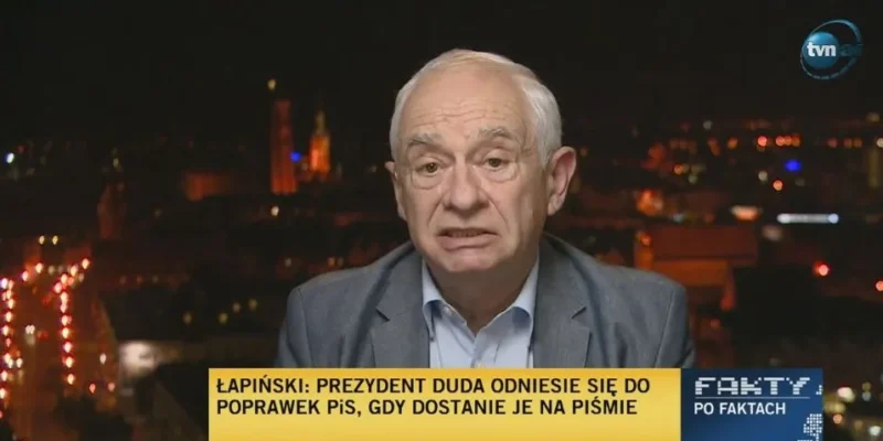 Starszy mężczyzna w marynarce udziela nocnego wywiadu w telewizji, z widocznym logo stacji i dolnym paskiem informacyjnym o prezydencie Dudzie i poprawkach PiS.