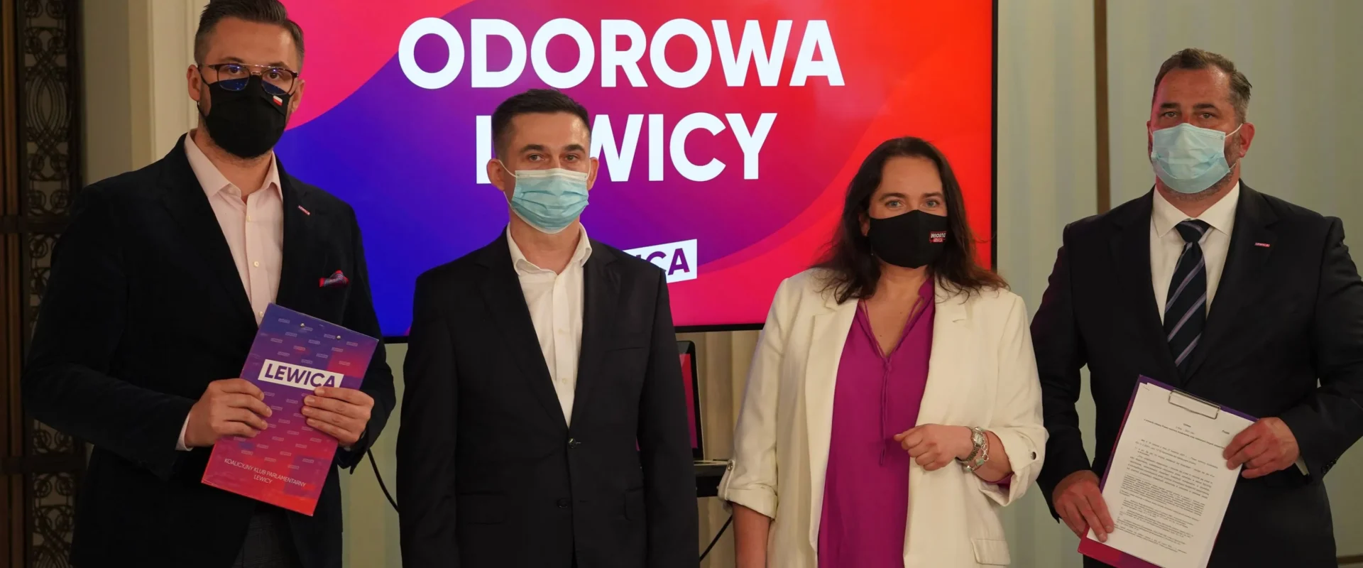 Czterech polityków Lewicy w garniturach i maseczkach stoi na konferencji prasowej, trzymając materiały promocyjne, przed ekranem z napisem „USTAWA ODOROWA LEWICY”.