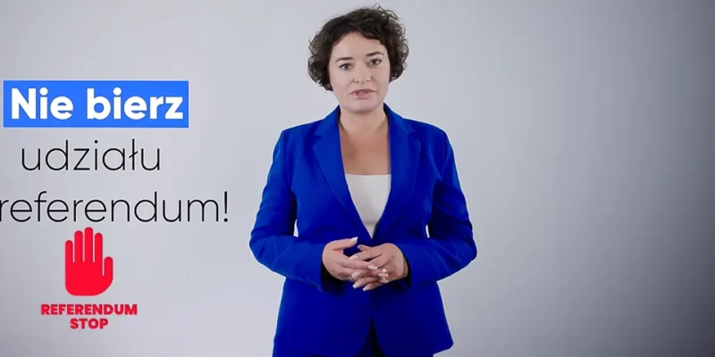 Kobieta w niebieskim garniturze stoi na szarym tle, obok widoczny jest napis Nie bierz udziału w referendum oraz czerwony symbol dłoni z napisem Referendum Stop.
