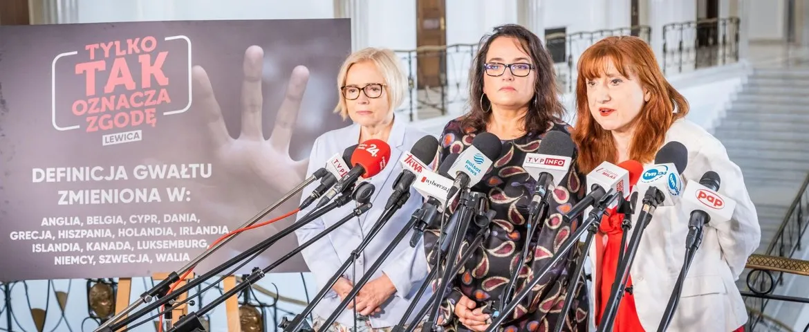 Trzy kobiety stoją przed mikrofonami w sali konferencyjnej, prezentując temat związany z definicją zgody i przemocy w kontekście ustawodawstwa.