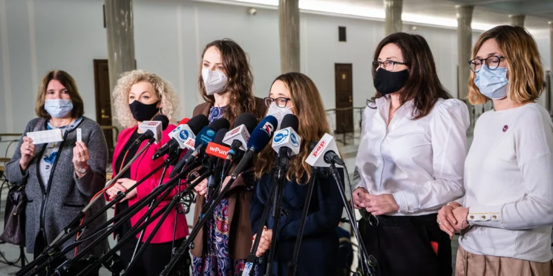 Grupa kobiet w maseczkach stoi za zestawem mikrofonów podczas konferencji prasowej o obowiązkowych testach na COVID-19 dla parlamentarzystów i pracowników Kancelarii Sejmu.