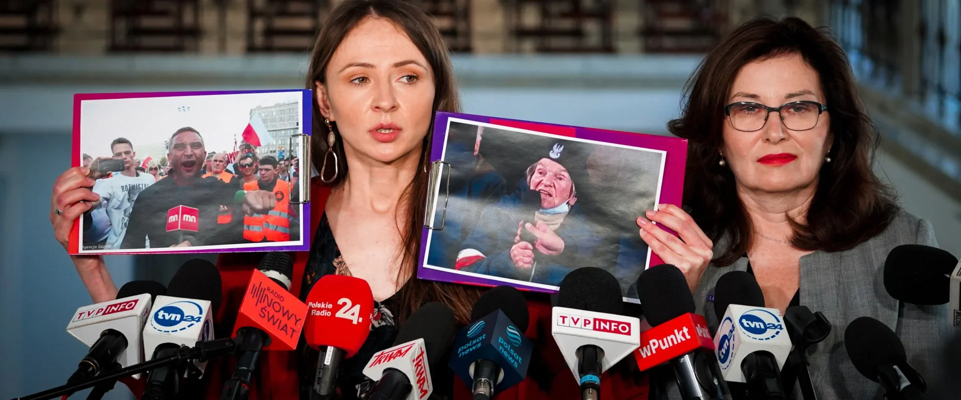 Na zdjęciu dwie kobiety prezentują zdjęcia podczas konferencji prasowej, w tle widać mikrofony i tłum ludzi.