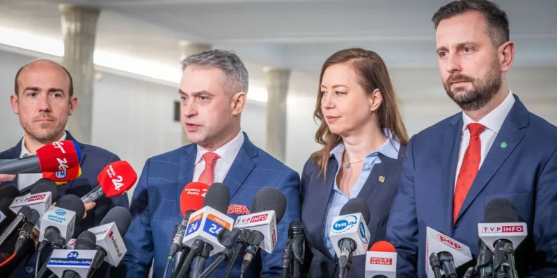 Czterech polityków stoi za mikrofonami podczas konferencji prasowej w budynku.