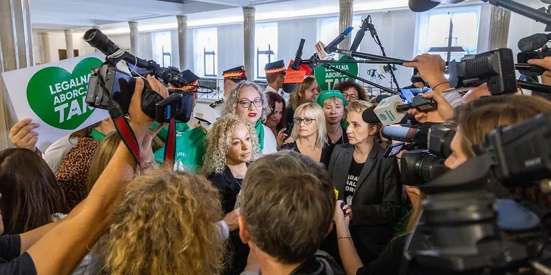 Kobiety w trakcie demonstracji w obronie legalizacji aborcji, otoczone przez tłum dziennikarzy i aparatów fotograficznych.