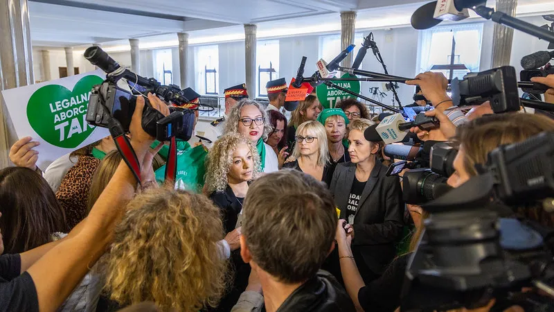 Kobiety w trakcie demonstracji w obronie legalizacji aborcji, otoczone przez tłum dziennikarzy i aparatów fotograficznych.