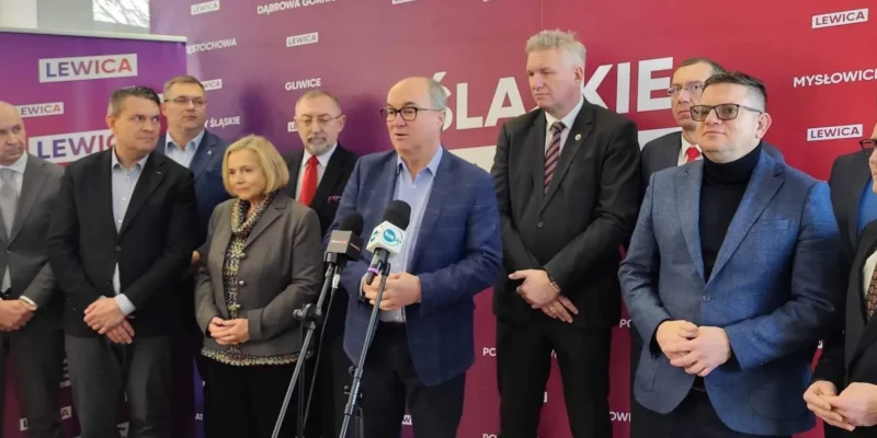 Na zdjęciu widać grupę mężczyzn i kobiet stojących razem przed bannerem z napisem "LEWICA", z jednym z mężczyzn mówiącym do mikrofonów.