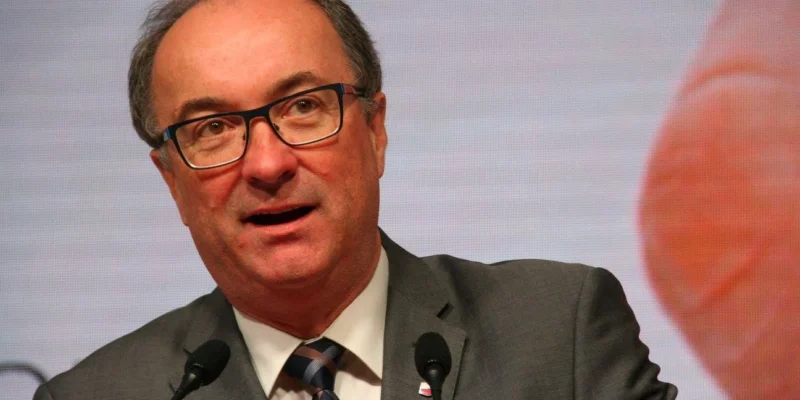 Mężczyzna w garniturze i okularach przemawia do dwóch mikrofonów podczas konferencji.