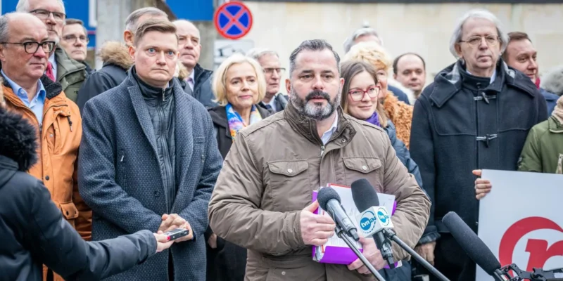Mężczyzna w brązowej kurtce przemawia do mikrofonów na konferencji prasowej, prezentując dokumenty złożone do rejestracji Komitetu obywatelskiej inicjatywy ustawodawczej „Renta Wdowia”.