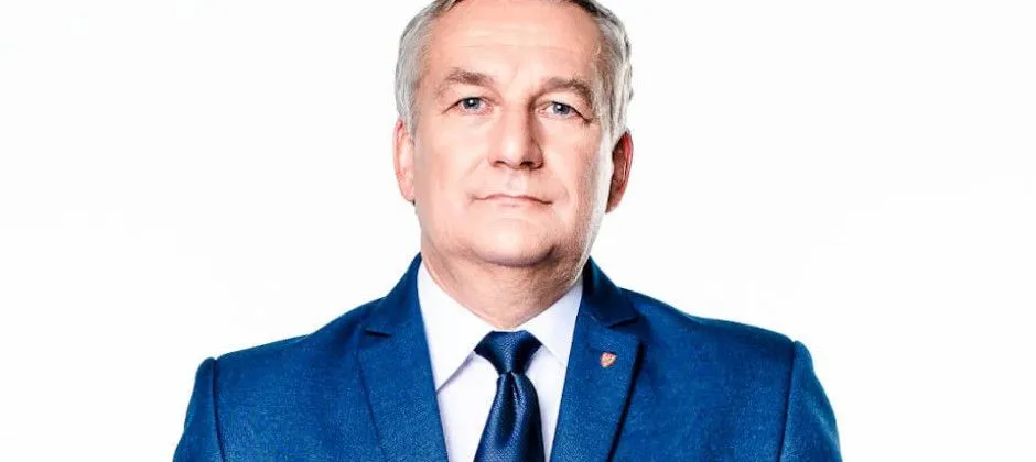 Portret mężczyzny w granatowym garniturze, białej koszuli i granatowym krawacie na białym tle.