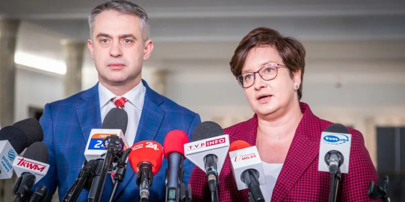 Na zdjęciu widoczna jest para polityków, mężczyzna i kobieta, którzy występują przed mikrofonami na konferencji prasowej.