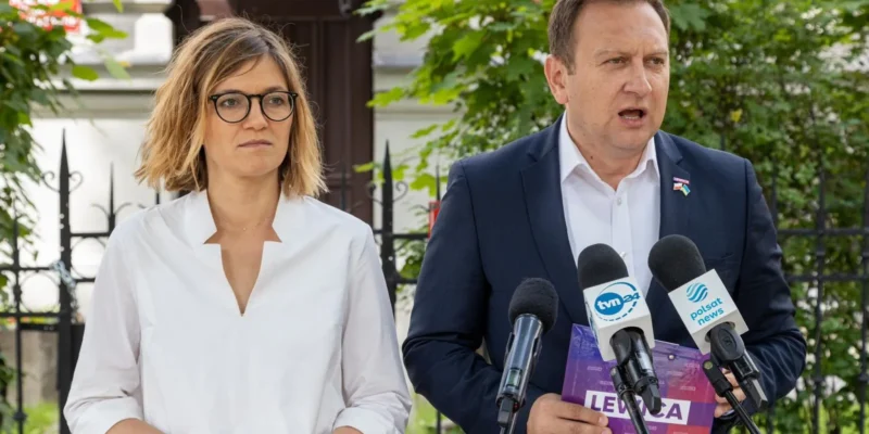 Dwóch polityków stoi na zewnątrz przed mikrofonami podczas konferencji prasowej o inflacji; kobieta w białej koszuli i okularach po lewej, mężczyzna w garniturze po prawej wygłasza oświadczenie, a w tle widać zieleń i ogrodzenie.