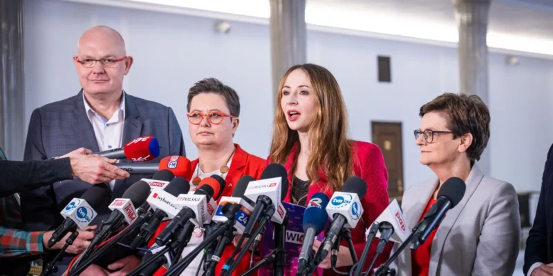 Grupa polityków przemawia na konferencji prasowej, otoczona licznymi mikrofonami.