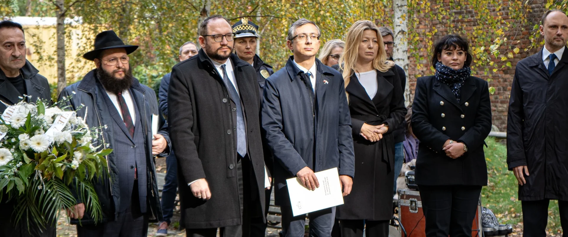 Grupa osób w formalnych ubraniach podczas uroczystej odsłonięcia tablicy upamiętniającej ofiary masowych egzekucji w Babim Jarze.