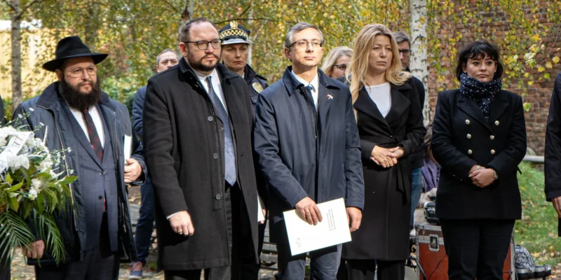 Grupa osób w formalnych ubraniach podczas uroczystej odsłonięcia tablicy upamiętniającej ofiary masowych egzekucji w Babim Jarze.