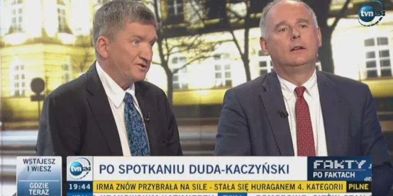 Dwóch mężczyzn w garniturach rozmawia w studiu telewizyjnym podczas programu informacyjnego, z paskiem informacyjnym na dole ekranu i logiem stacji w prawym górnym rogu.
