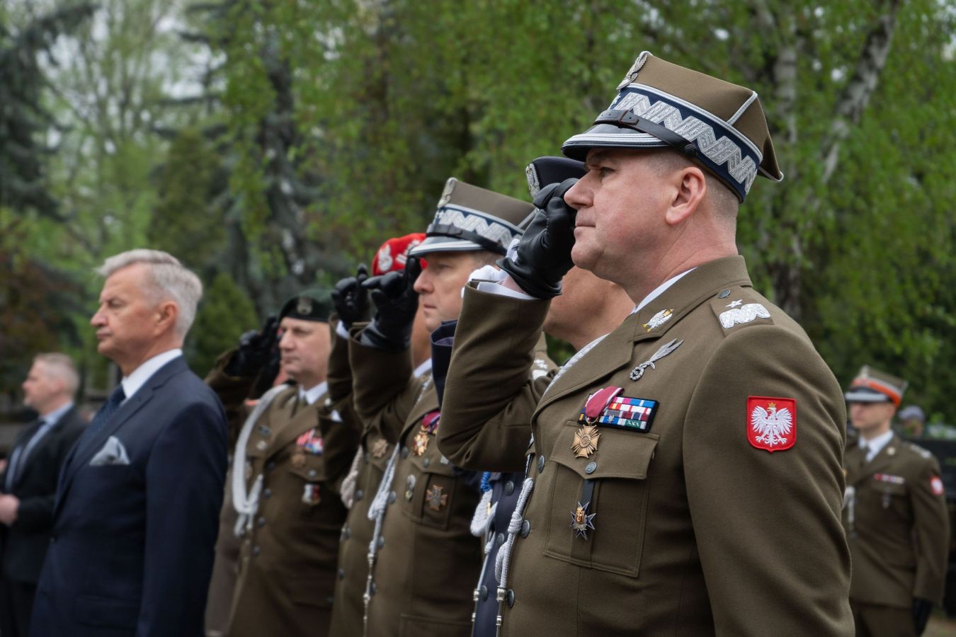 Grupa polskich żołnierzy w mundurach składa salut podczas uroczystości upamiętniającej 14. rocznicę katastrofy smoleńskiej, na tle zieleni.
