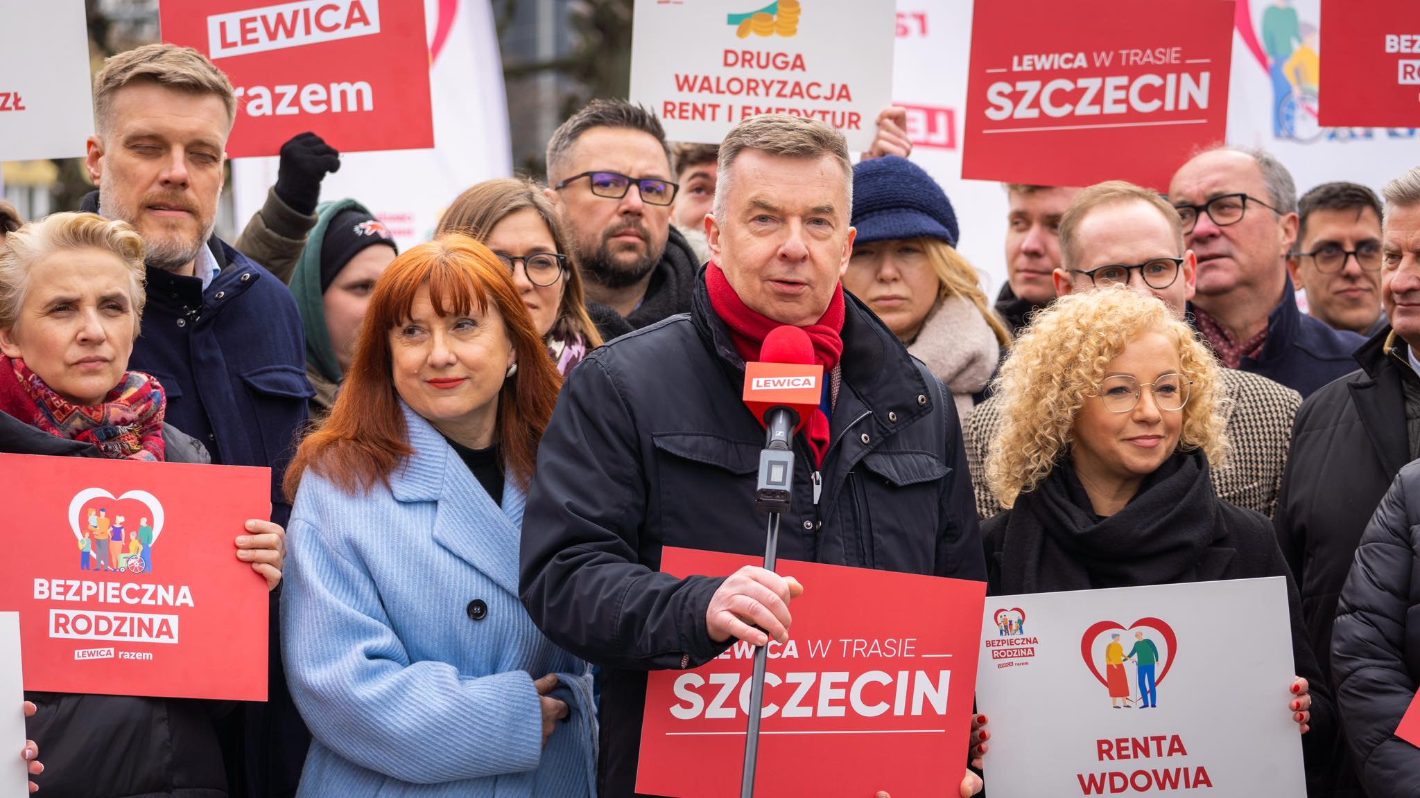 Na zdjęciu widać grupę osób trzymających kolorowe banery z hasłami dotyczącymi polityki społecznej w Szczecinie.