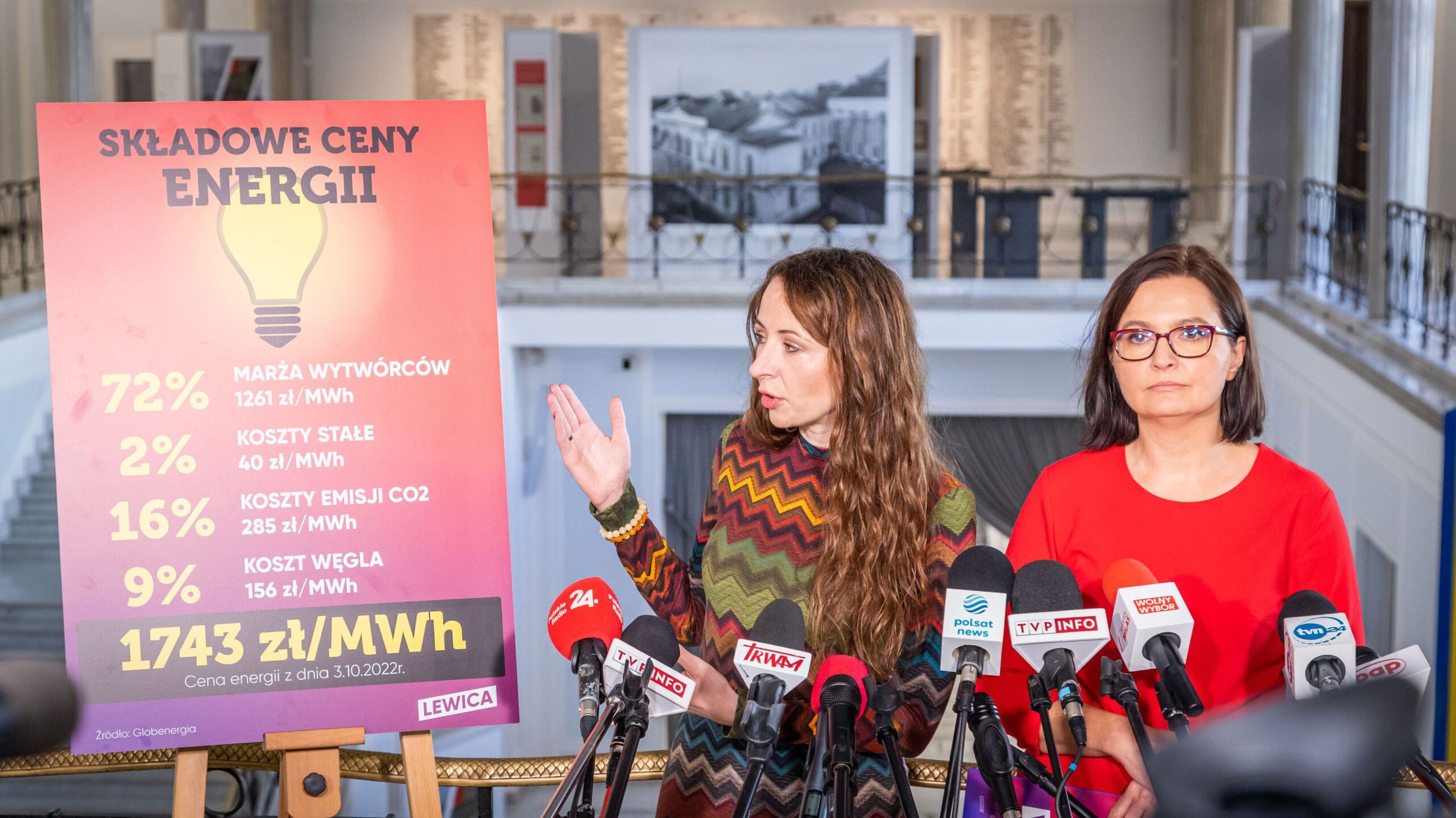 Na zdjęciu przedstawiono konferencję prasową, na której dwie kobiety omawiają szczegóły dotyczące składników cen energii, z widoczną planszą informacyjną.