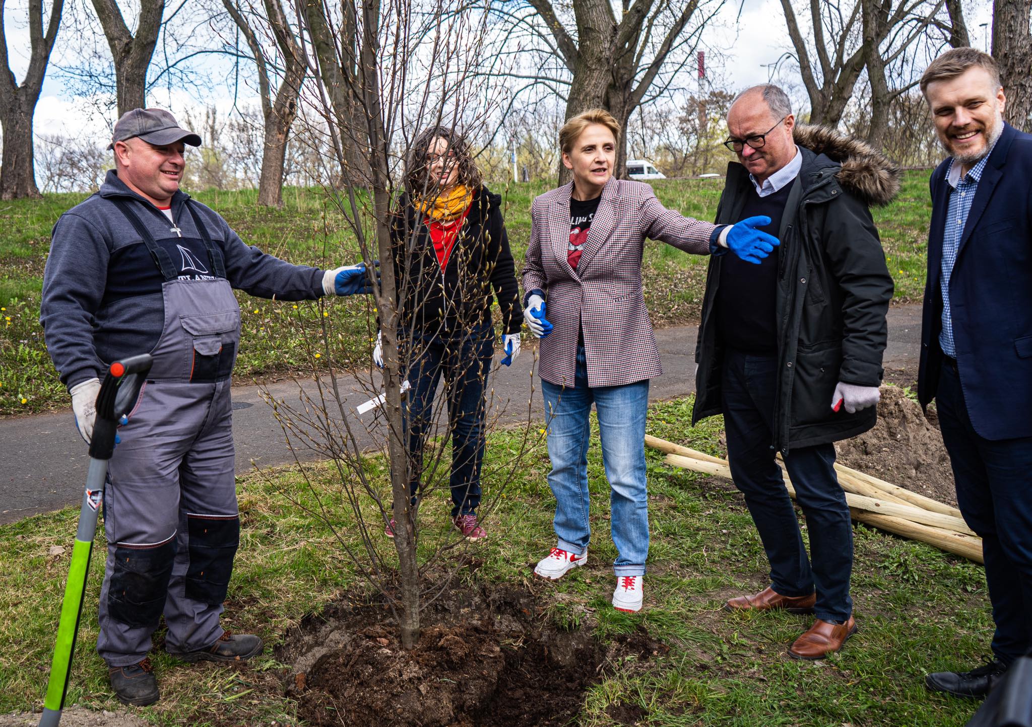 Na zdjęciu grupa osób bierze udział w sadzeniu drzewa w parku.