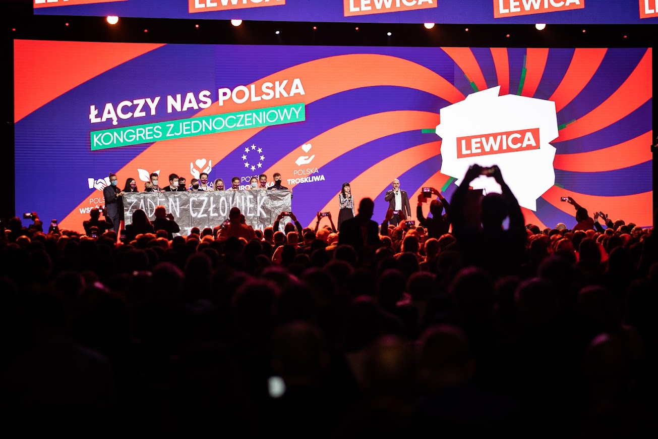 Duża scena kongresu zjednoczeniowego Nowej Lewicy z kolorowym tłem z napisem „Łączy nas Polska” i tłumem zgromadzonych widzów przed nią.
