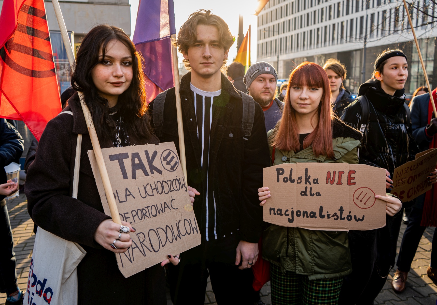 Na zdjęciu widoczni są młodzi ludzie trzymający transparenty podczas manifestacji, z hasłami wspierającymi uchodźców i sprzeciwiającymi się nacjonalizmowi.