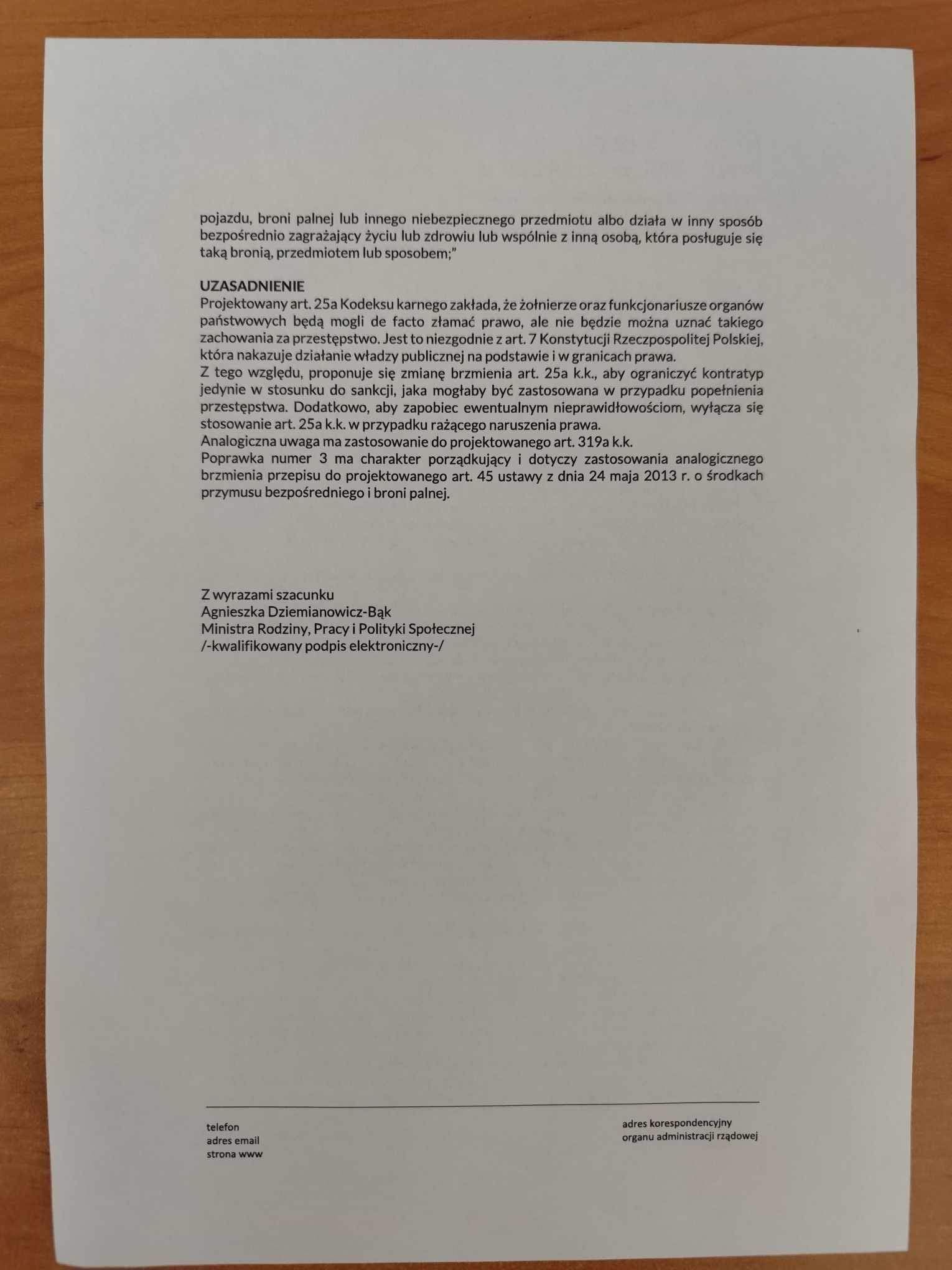 Strona dokumentu w języku polskim z nagłówkiem UZASADNIENIE i podpisem na dole, leżąca na drewnianym blacie.