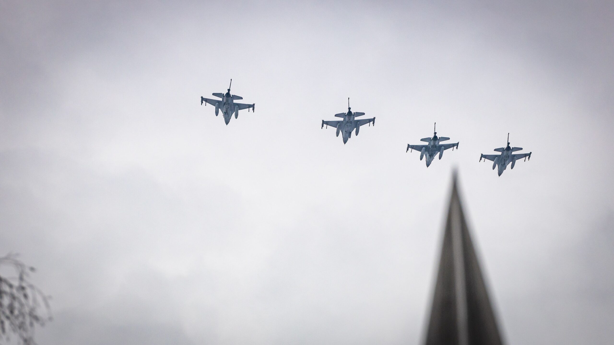 Na zdjęciu widać cztery myśliwce przelatujące nad chmurami, z widocznym w dolnej części kontrastującym szpice.