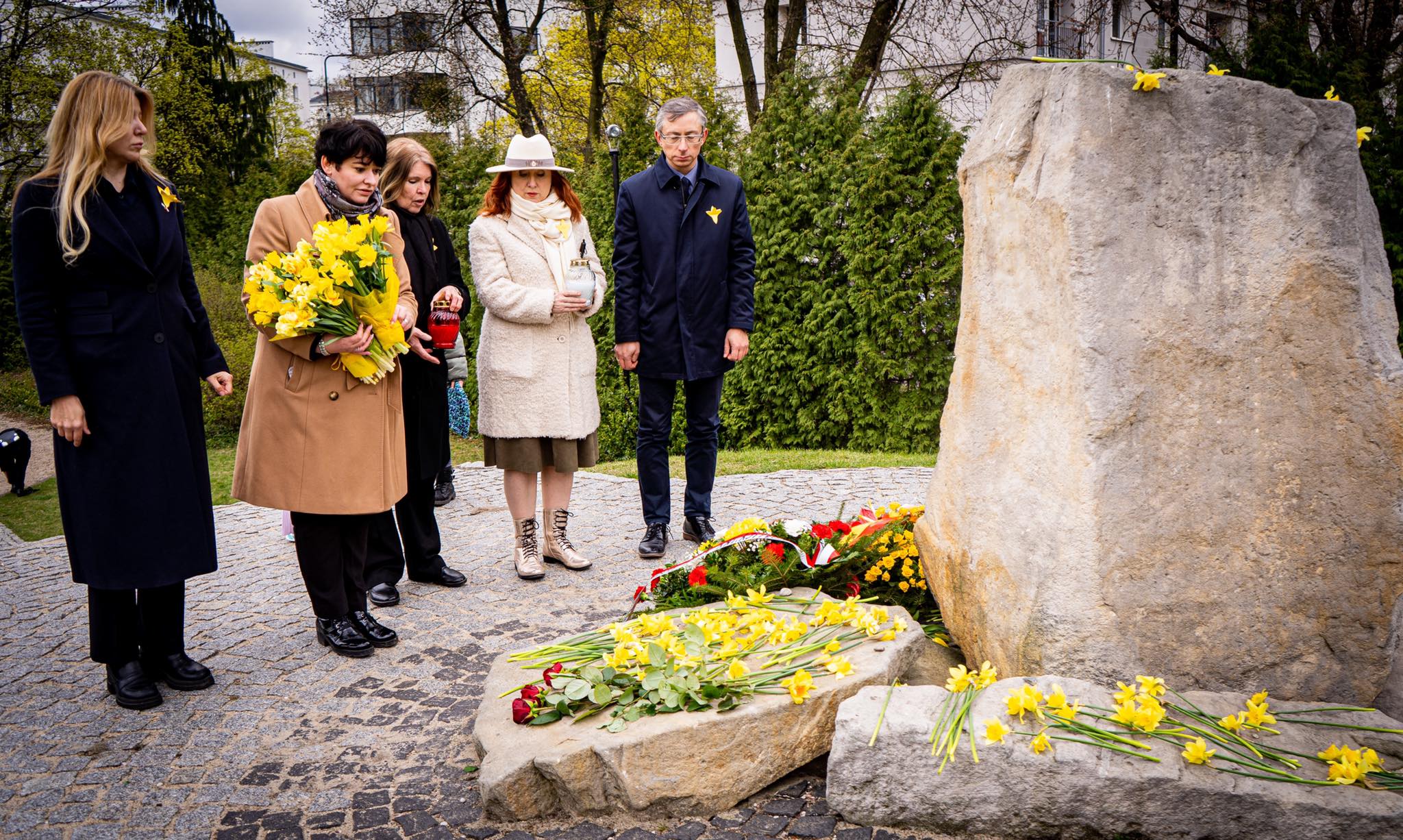 Grupa osób składa kwiaty przed kamiennym pomnikiem podczas obchodów 79. rocznicy Powstania w Getcie Warszawskim.