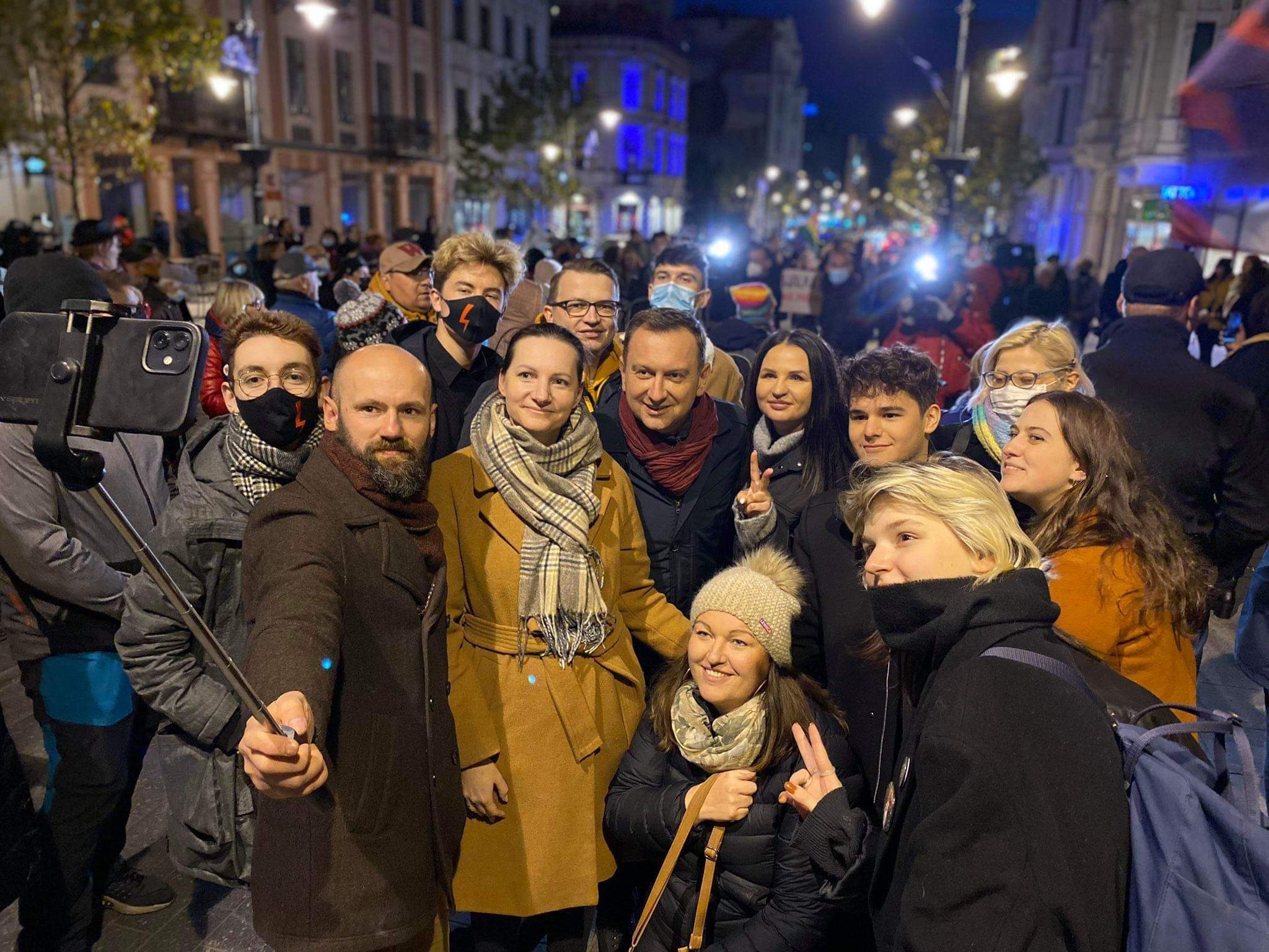 Grupa osób pozująca do selfie podczas wieczornego protestu na ulicach miasta.