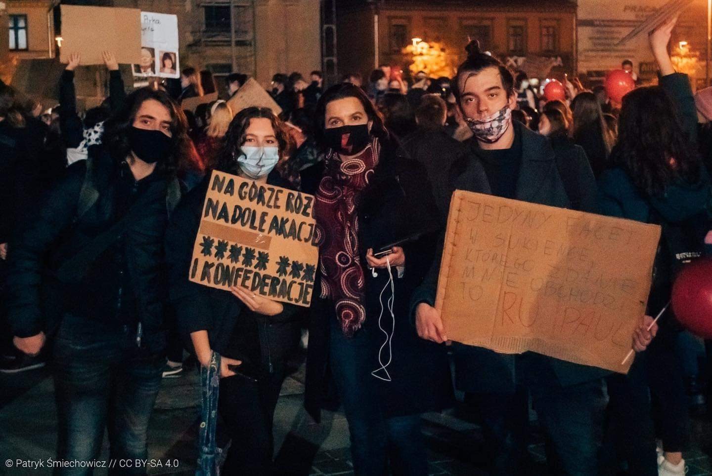 Na zdjęciu widać grupę młodych ludzi z transparentami podczas protestu w ciemnym otoczeniu.
